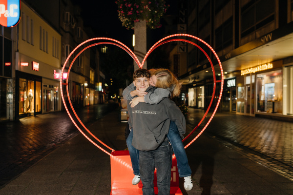 ein Mädchen küsst einen Jungen vor einem Metallherz auf die Wange