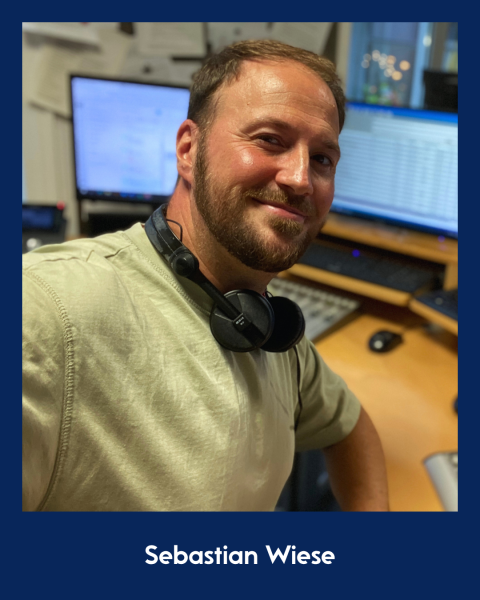 Mann mit Bart und Kopfhörern im Radiostudio lächelt in Kamera.