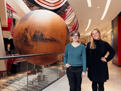 Zwei Mitarbeiterinnen der Wissenswerkstadt stehen vor dem Modell des Mars. 