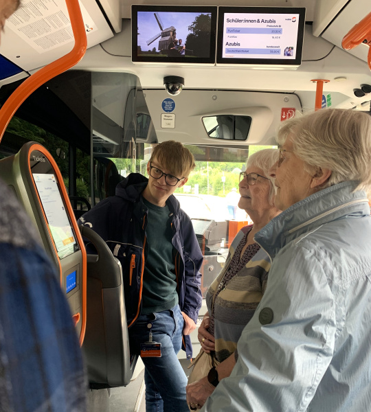 Ein Mitarbeiter von moBiel erklärt zwei Seniorinnen den neuen Fahrkartenautomat im Bus.