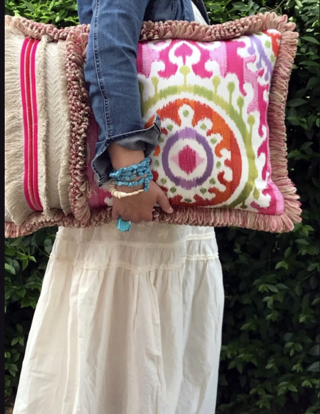 Bildausschnitt zeigt Frau mit weißem Rock und Jeansjacke mit buntem Kissen unter dem Arm