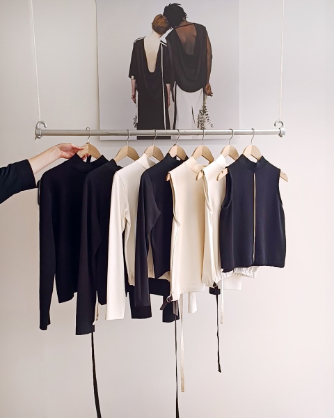 Aufnahme zeigt schwarze und weiße Kleidung auf einer Holzstange. Minimalistisch pur vor weißer Wand