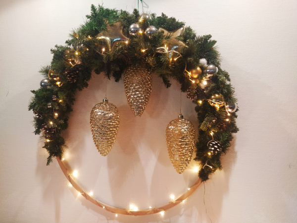 Ein Adventskranz an der Wand mit goldenen Tannenzapfen