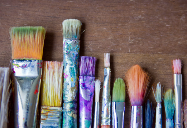 Auf dem Bild sind verschiedene Pinsel in unterschiedlicher Größe und mit bunten Farbresten zu sehen.