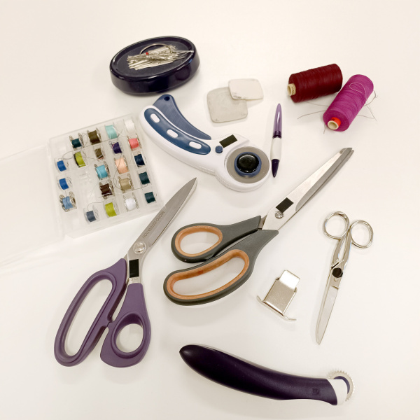 Nähmaterialien auf weißem Untergrund: Scheren, Garne, Spulen, Nadeln.
