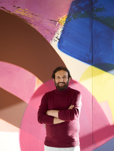 Der Künstler Aatifi steht vor einer farbenfrohen Malerei