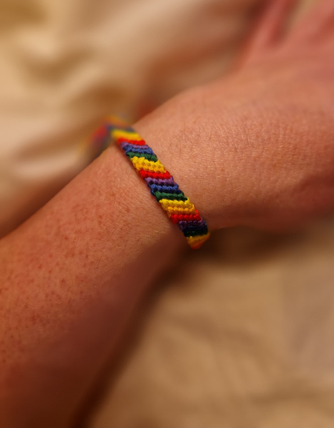 Das Bild zeigt ein geknüpftes Armband in Regenbogenfarben an einem Handgelenk.