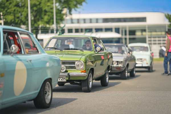 Mehrere Oldtimer fahren im Sonnenschein auf das LENKWERK Gelände ein. Im Vordergrund ein markanter g