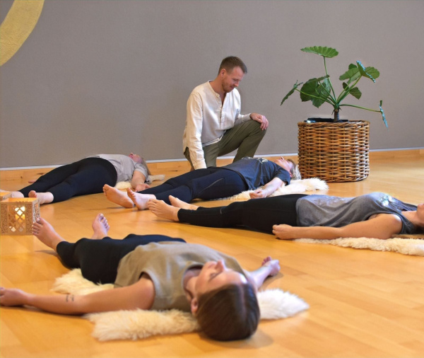 Teilnehmende liegen entspannt. Ein Kursleiter begleitet sie bei einer Breathwork-Session.