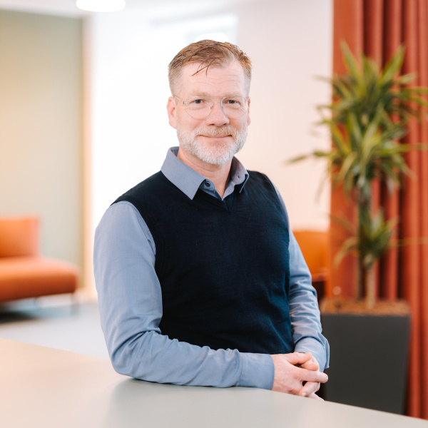 Mann in dunklem Pullover und hellblauem Hemd steht am Schreibtisch im modernen Büro.