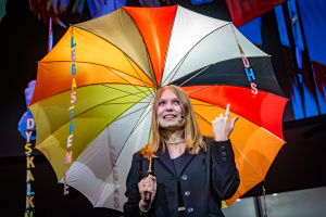 Eine junge Frau hält einen bunten Schirm auf der Bühne.